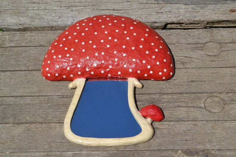 Pu&ograve; includere: Uno specchio a forma di fungo rosso e bianco a pois con una superficie riflettente blu. Lo specchio &egrave; fatto di cartapesta e ha un gambo bianco.