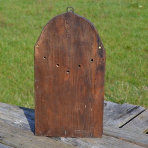 May include: The back of a wooden box with a rounded top. The box is made of dark brown wood and has a few small holes in it. The box is sitting on a wooden surface.
