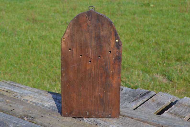 May include: The back of a wooden box with a rounded top. The box is made of dark brown wood and has a few small holes in it. The box is sitting on a wooden surface.