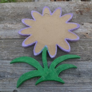 May include: A handmade flower decoration with a light purple outline and a tan center. The flower is separated from the green leaves and stem. The flower and leaves are made of a textured material, possibly paper mache.