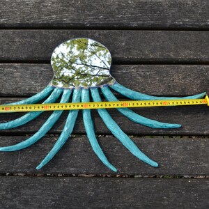 May include: A turquoise octopus-shaped mirror with a reflective surface, resting on a wooden surface. The octopus's tentacles extend, and a measuring tape shows a length of approximately 30 inches.