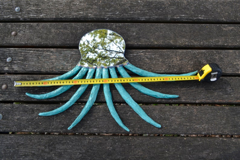 May include: A turquoise octopus-shaped mirror with a reflective surface, resting on a wooden surface. The octopus's tentacles extend, and a measuring tape shows a length of approximately 30 inches.