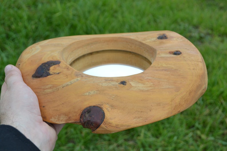 Puede incluir: Un espejo de madera con un acabado de madera natural y un espejo redondo insertado. El espejo est&aacute; rodeado por un marco de madera grueso e irregular.