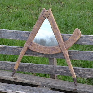 May include: A wooden compass mirror with a brown and gold finish. The mirror is shaped like a triangle and has a round hole in the top. The compass is hanging on a wooden fence.
