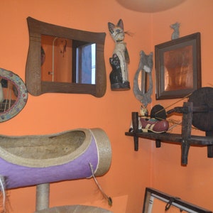 May include: A room decorated with a variety of cat-themed items, including a cat-shaped mirror, a cat-shaped figurine, and a cat bed. The room also features a spinning wheel and a shelf with various items.