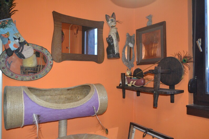 May include: A room decorated with a variety of cat-themed items, including a cat-shaped mirror, a cat-shaped figurine, and a cat bed. The room also features a spinning wheel and a shelf with various items.