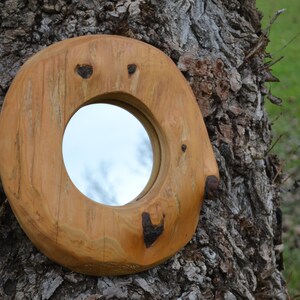 Puede incluir: Un espejo redondo de madera con un acabado de madera natural. El espejo est&aacute; tallado con formas de coraz&oacute;n alrededor del borde y est&aacute; montado en un tronco de &aacute;rbol.