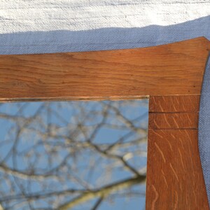 May include: A wooden mirror frame with a curved top and a reflection of a tree branch against a blue sky.
