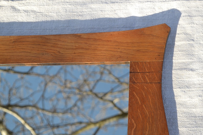 May include: A wooden mirror frame with a curved top and a reflection of a tree branch against a blue sky.