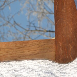 May include: Close-up of a wooden mirror frame with a natural wood finish. The frame has a curved edge and is made of solid wood.