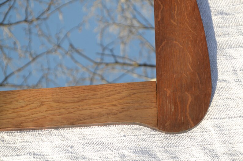 May include: Close-up of a wooden mirror frame with a natural wood finish. The frame has a curved edge and is made of solid wood.