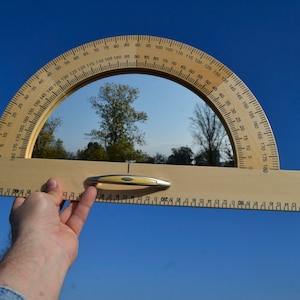 May include: A wooden protractor with a clear plastic window, showing a reflection of trees and a blue sky. The protractor has markings in degrees from 0 to 180.