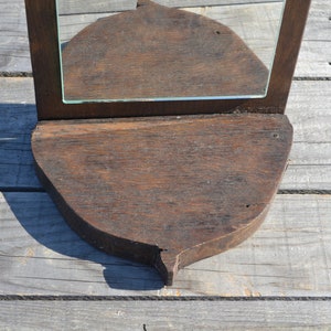 May include: A dark brown wooden mirror with a beveled glass mirror and a shelf. The shelf is shaped like a leaf and has a pointed tip.