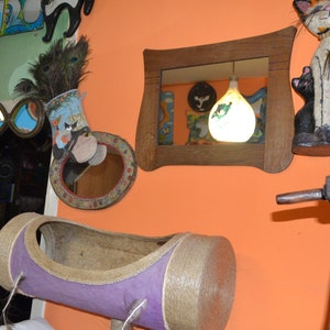 May include: A room decorated with various items, including a cat-shaped figurine, a mirror, a lamp, and a cat bed. The walls are painted a bright orange color.