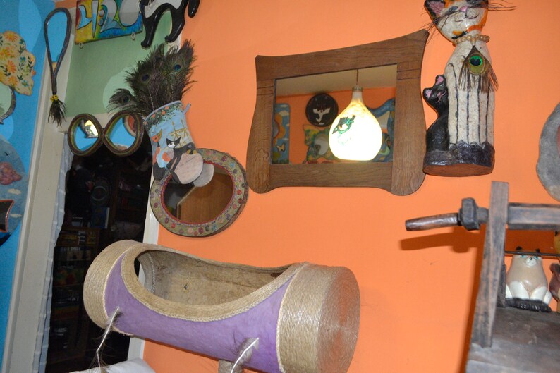 May include: A room decorated with various items, including a cat-shaped figurine, a mirror, a lamp, and a cat bed. The walls are painted a bright orange color.