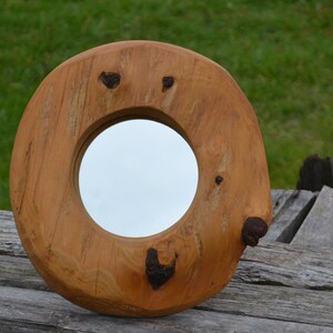 Puede incluir: Un espejo redondo de madera con un acabado de madera natural. El espejo est&aacute; encajado en un marco de madera grueso e irregular con nudos y patrones de veta.