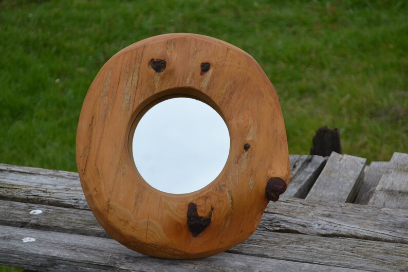 Puede incluir: Un espejo redondo de madera con un acabado de madera natural. El espejo est&aacute; encajado en un marco de madera grueso e irregular con nudos y patrones de veta.