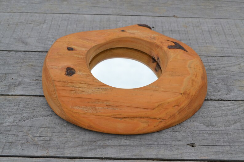 Puede incluir: Un espejo redondo de madera con un acabado de madera natural. El espejo est&aacute; encajado en un marco de madera grueso e irregular, con un aspecto r&uacute;stico.