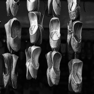 May include: A display of black leather shoes with intricate designs hanging from a string. The shoes are pointed and have a decorative strap across the top.