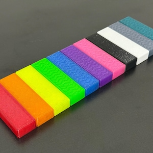 May include: A collection of colorful, rectangular blocks arranged diagonally. The blocks display a spectrum of colors, including red, orange, yellow, green, blue, purple, pink, black, white, gray, and teal. Each block has a textured surface.