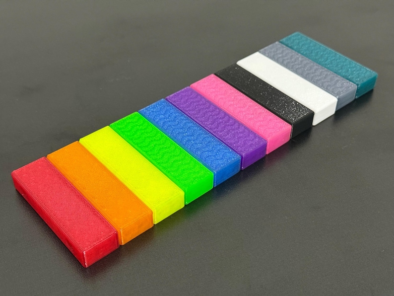 May include: A collection of colorful, rectangular blocks arranged diagonally. The blocks display a spectrum of colors, including red, orange, yellow, green, blue, purple, pink, black, white, gray, and teal. Each block has a textured surface.