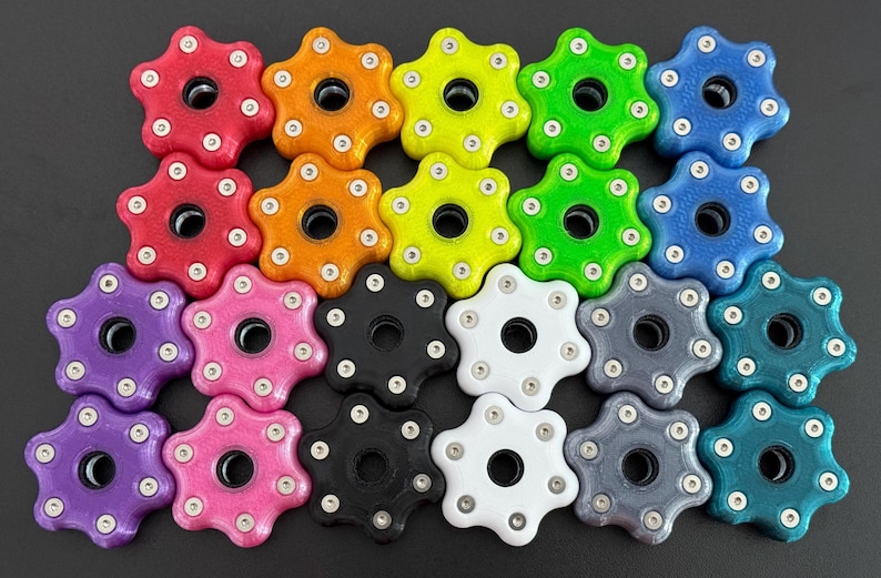 May include: A collection of colorful, star-shaped knobs in various colors, including red, orange, yellow, green, blue, purple, pink, black, white, gray, and teal. Each knob has a central hole and is adorned with small silver accents.