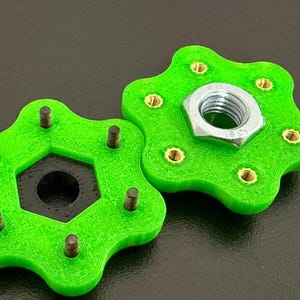 May include: Two bright green, star-shaped components with brass inserts and a hexagonal center. One component has a silver nut attached. The objects are on a dark surface.
