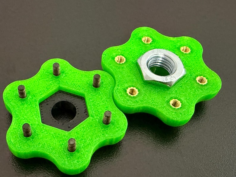 May include: Two bright green, star-shaped components with brass inserts and a hexagonal center. One component has a silver nut attached. The objects are on a dark surface.