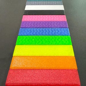 May include: A collection of rectangular, textured blocks arranged in a stepped pattern. The blocks display a spectrum of colors, including red, orange, yellow, green, blue, purple, pink, black, white, and teal. The blocks have a slightly granular appearance.