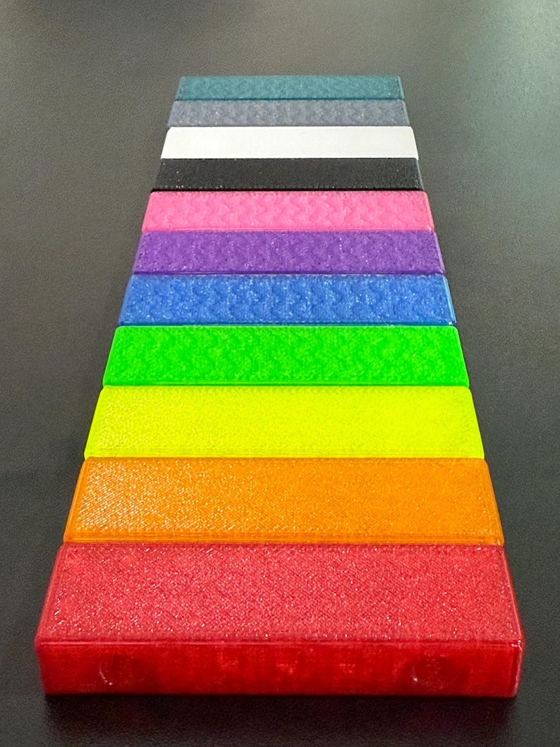 May include: A collection of rectangular, textured blocks arranged in a stepped pattern. The blocks display a spectrum of colors, including red, orange, yellow, green, blue, purple, pink, black, white, and teal. The blocks have a slightly granular appearance.