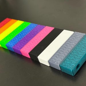 May include: A collection of colorful, rectangular blocks arranged in a row. The blocks display a rainbow of colors, transitioning from red to teal, with a textured surface. Each block has a rectangular shape with rounded edges.