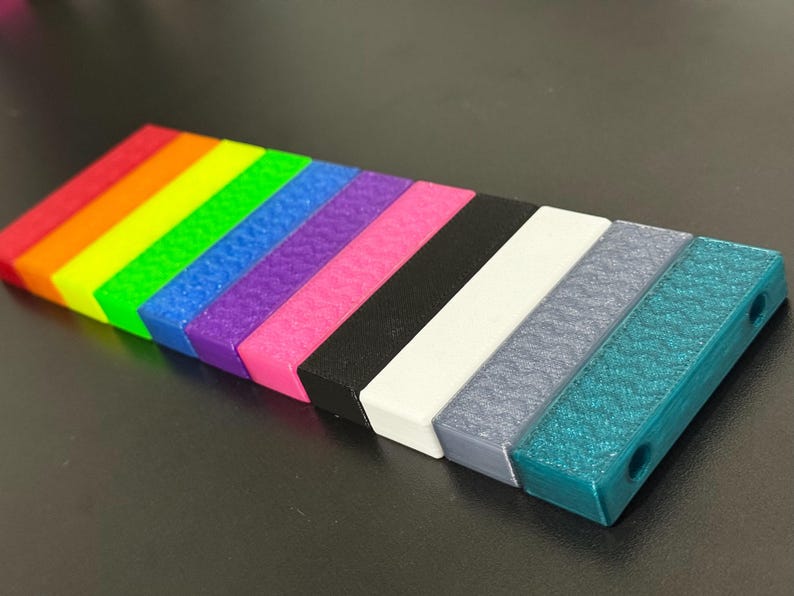 May include: A collection of colorful, rectangular blocks arranged in a row. The blocks display a rainbow of colors, transitioning from red to teal, with a textured surface. Each block has a rectangular shape with rounded edges.