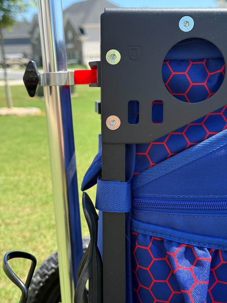 May include: Close-up of a black metal frame with a blue bag featuring a red honeycomb pattern. The frame has a circular cutout and is attached to a silver pole with a black knob. A red lever is visible. The bag has a blue strap.