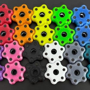 May include: A collection of colorful, star-shaped knobs in various colors, including red, orange, yellow, green, blue, purple, pink, black, white, gray, and teal. Each knob has a central hole and small black dots around the edges.