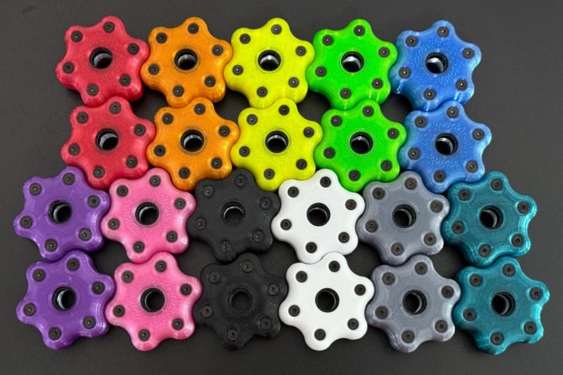 May include: A collection of colorful, star-shaped knobs in various colors, including red, orange, yellow, green, blue, purple, pink, black, white, gray, and teal. Each knob has a central hole and small black dots around the edges.