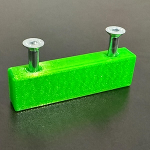 May include: A bright green rectangular object with two silver screws inserted. The screws have a flat, hexagonal head. The object is likely a component or part for a larger item.