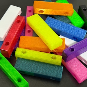 May include: A collection of colorful, rectangular blocks in various shades including red, orange, green, blue, and purple. Each block has two circular holes. The blocks are scattered, creating a vibrant and playful display.
