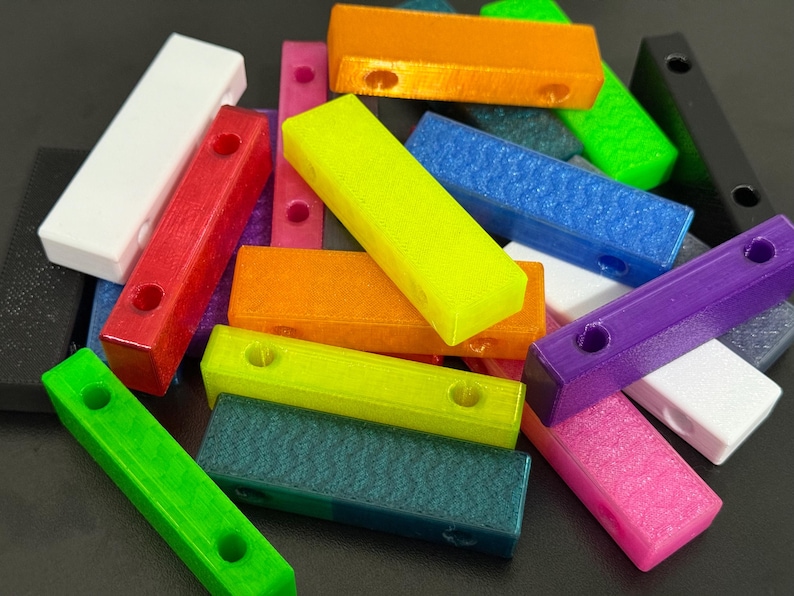 May include: A collection of colorful, rectangular blocks in various shades including red, orange, green, blue, and purple. Each block has two circular holes. The blocks are scattered, creating a vibrant and playful display.