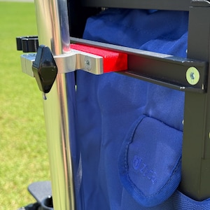 May include: Close-up of a utility wagon frame with a blue fabric interior. The frame is black with silver metal accents, including a vertical pole and a red support piece. The wagon has a black handle and black wheels.