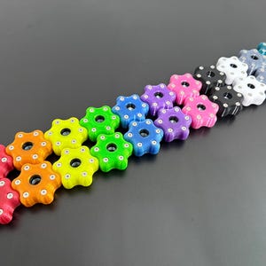 May include: A collection of colorful, star-shaped knobs in various colors, including red, orange, yellow, green, blue, purple, pink, black, white, and teal. Each knob has a central hole and small circular indentations around the edges.