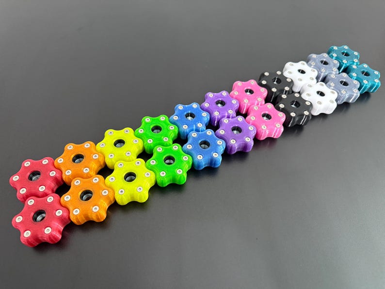 May include: A collection of colorful, star-shaped knobs in various colors, including red, orange, yellow, green, blue, purple, pink, black, white, and teal. Each knob has a central hole and small circular indentations around the edges.