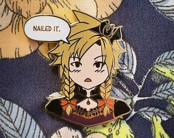 Pode incluir: Um alfinete de esmalte em estilo cartoon com um personagem de cabelo loiro e tranças. O personagem está vestindo uma roupa preta e roxa com detalhes em laranja. Um balão de fala acima do personagem diz "NAILED IT."