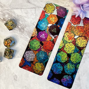 Könnte beinhalten: Zwei farbenfrohe Lesezeichen mit einem sich wiederholenden Muster aus regenbogenfarbenen zwanzigseitigen Würfeln. Die Würfel sind schwarz umrandet und haben weiße Zahlen.