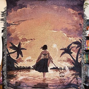 May include: A woven tapestry throw blanket featuring a sunset scene with a woman in a long dress standing in the water. The woman is holding a staff with a glowing orb at the end. Two palm trees are on either side of the woman. The background is a sunset with clouds and a light blue sky.