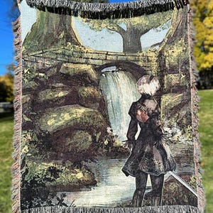 Könnte beinhalten: Ein gewebter Wandteppich mit einer Frau, die in einer Waldlandschaft steht. Die Frau trägt ein schwarzes Kleid und hat weißes Haar. Sie steht vor einem Wasserfall und einer Brücke. Der Wandteppich ist aus verschiedenen Farben gefertigt, darunter Grün, Braun und Blau.