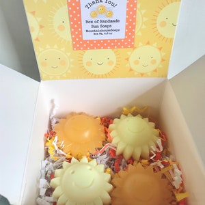 May include: A white box with a yellow and orange sun pattern on the lid. The box contains four handmade sun-shaped soaps. The lid has a label that says "Thank You! Box of Handmade Sun Soaps MountainhouseSoaps Net Wt. 4.6 oz."