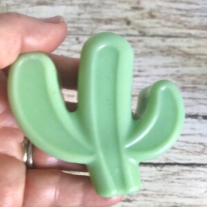 May include: A green plastic cactus shaped like a saguaro cactus with two arms.