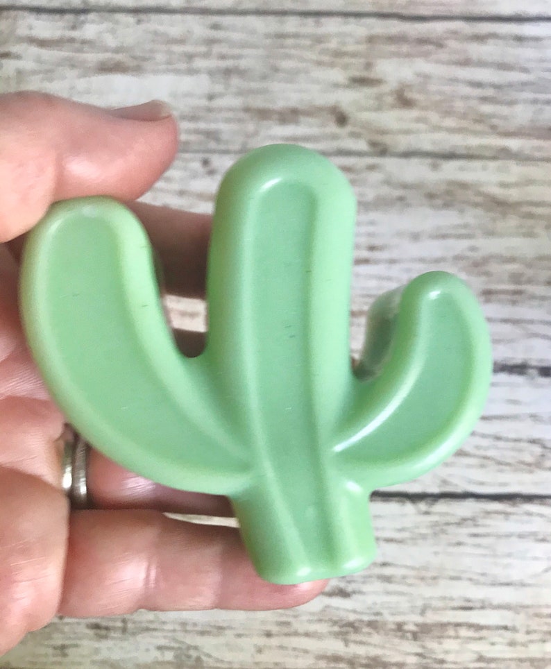 May include: A green plastic cactus shaped like a saguaro cactus with two arms.