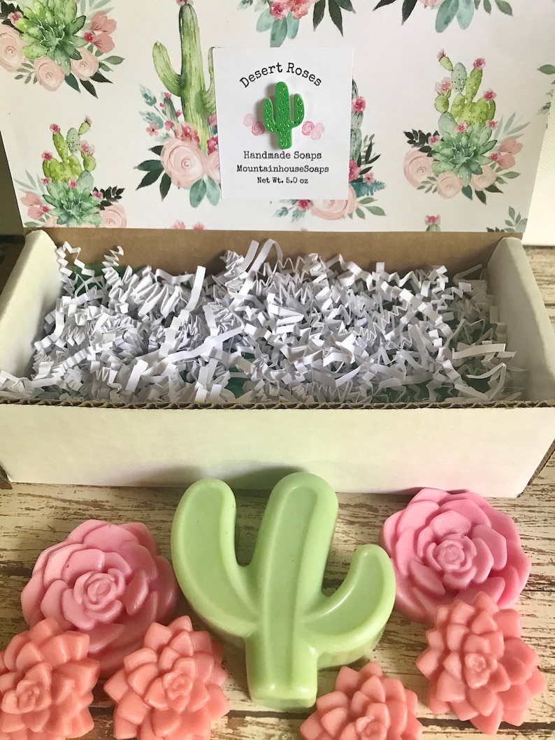 May include: A gift box filled with handmade soaps featuring a cactus and succulent design. The soaps are green, pink, and white. The box is decorated with a floral pattern and the text "Desert Roses Handmade Soaps MountainhouseSoaps Net Wt. 5.0 oz".