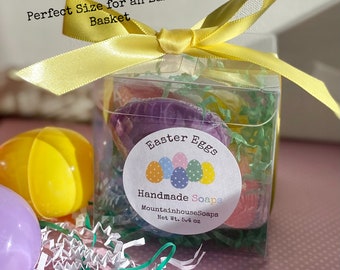 May include: A clear plastic box filled with colorful handmade soap eggs, tied with a yellow ribbon. The box has a label that reads "Easter Eggs Handmade Soaps MountainhouseSoaps Net Wt. 5.4 oz".
